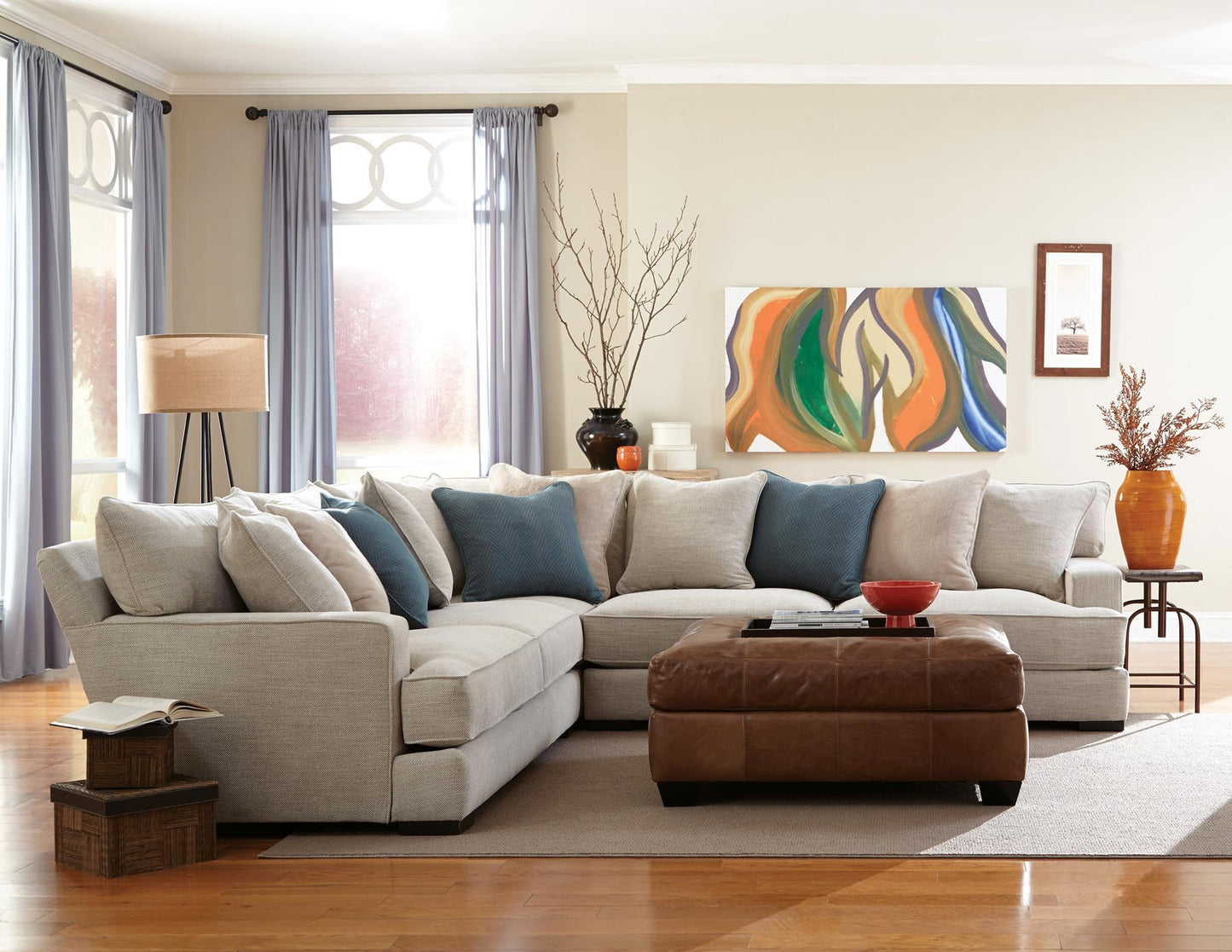 MATHIS sectional with accent pillows and leather ottoman in a living room
